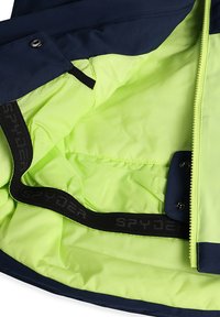 Die Innenseite der marineblauen und fluoreszierend gelben Jacke bietet eine glatte Textur, einen kontrastierenden Reißverschluss und einen schwarzen "SPYDER" Logo-Gurt.