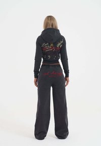 Svart kort hoodie med broderad text, parat med matchande vida byxor som har en logotyp. Båda har en mjuk, texturerad finish.