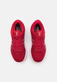 Dvojice červených běžeckých bot Asics viděná zhora s síťovinovou textilií, bílými mezipodešvemi a tkaničkovým zapínáním na bílém pozadí.