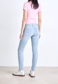 Ljust blå jeans i slim fit med bakfickor, kombinerat med en rosa åtsittande t-shirt och silverfärgade sneakers, mot en neutral bakgrund.