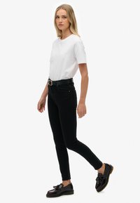 Jeans skinny negros combinados con una camiseta blanca, de corte ajustado, textura de denim y un cinturón negro con una hebilla dorada.