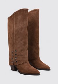 Botas de ante marrón hasta la rodilla con punto afilado y tacón de bloque. Con detalles de cordones laterales con ojales de metal y parte superior ligeramente acampanada.