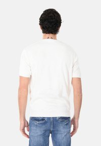 Maglione bianco a maniche corte in maglia con collo a costine e texture liscia, indossato con jeans di denim blu, visto da dietro.