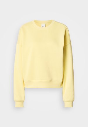 Žlutá krátká mikina z měkké látky, s kulatým výstřihem, dlouhými rukávy a žebrovanými manžetami. Hladký jednobarevný povrch bez vzorů.