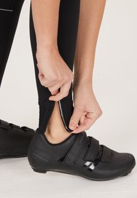 Zwarte fietschoenen met klittenbandsluitingen en geperforeerde details. Zwart met rits leggings worden bij de enkel aangepast.
