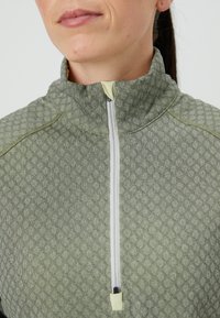 Pullover com zíper de um quarto em tecido texturizado verde claro com padrão de diamante, apresentando um zíper branco e um acabamento claro na gola.
