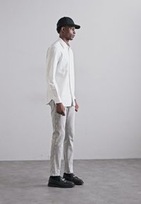 Chemise blanche à manches longues, pantalon slim gris clair, mocassins noirs et casquette noire. Tissu doux avec un design simple et des couleurs neutres.