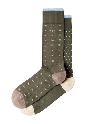 Par de calcetines verde oliva con puños azules, talones y dedos beige; un calcetín tiene un pequeño patrón de "H", el otro está salpicado de pequeñas cruces.