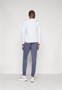 Long-sleeve white shirt with a subtle logo on the back, paired with gray tapered pants and gray athletic shoes with orange accents.