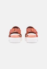 Orange fabric sandals with adjustable straps and white rubber soles, featuring a circular logo detail on the back strap.