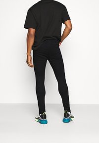 Jeans neri aderenti con vita alta, abbinati a una t-shirt nera fluida e sneakers colorate con suola blu.