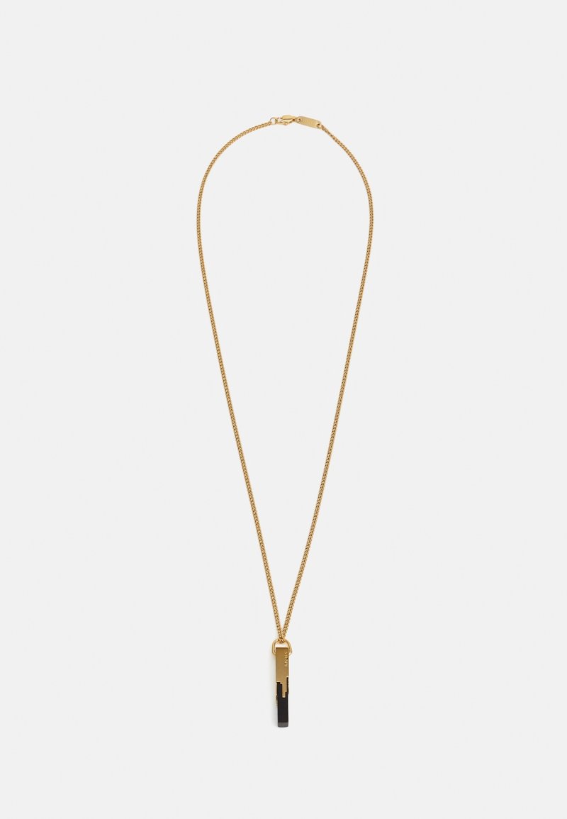 Collier délicat en chaîne d'or avec un pendentif rectangulaire noir et or suspendu au centre sur un fond uni.