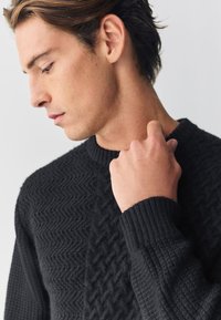 Čierny pletený sveter s textúrovanými cik-cak vzormi na prednej strane, rebrovaným lemom a manžetami, s klasickým okrúhlym výstrihom.