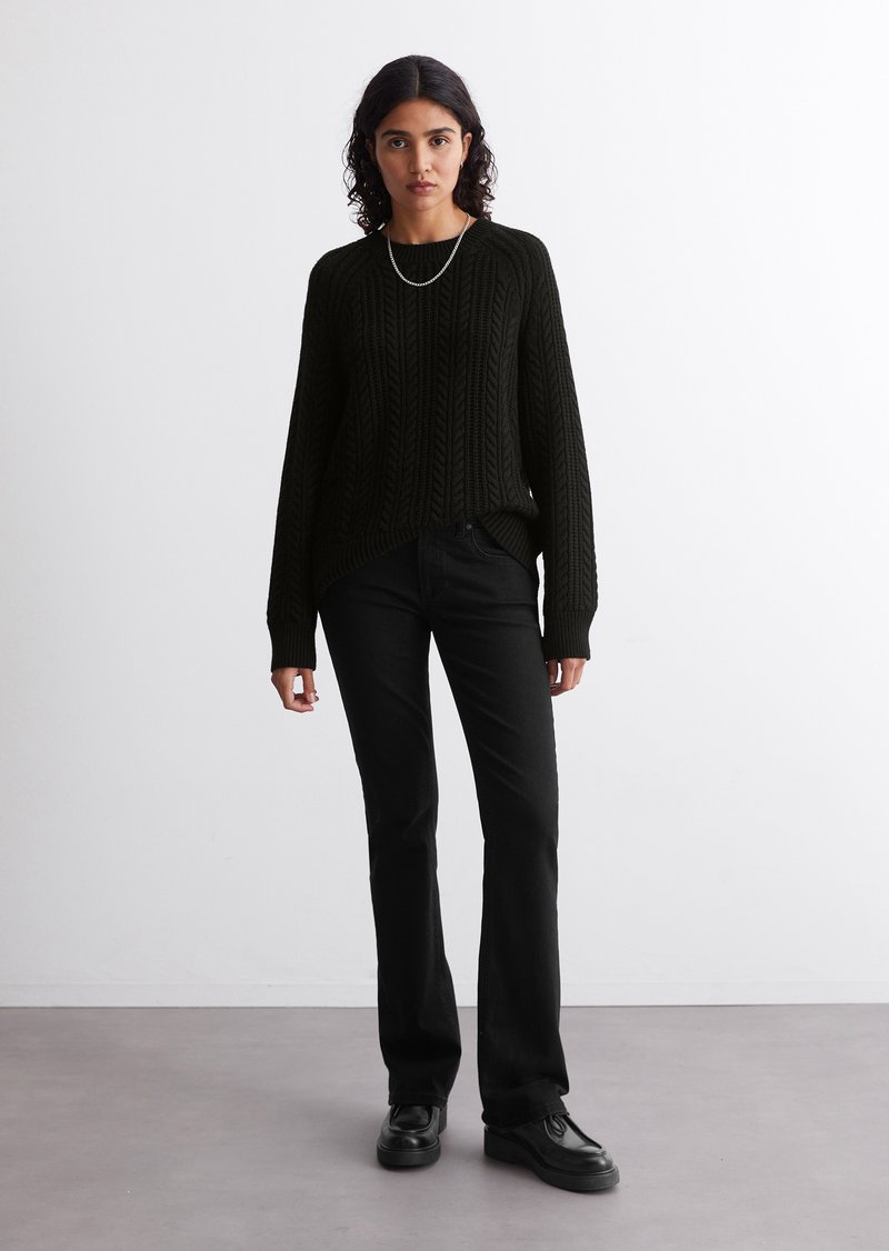 Schwarzer Strickpullover mit strukturiertem Muster, lockere Passform, lange Ärmel, kombiniert mit schwarzen geraden Jeans und schwarzen Schuhen. Einfache silberne Halskette.