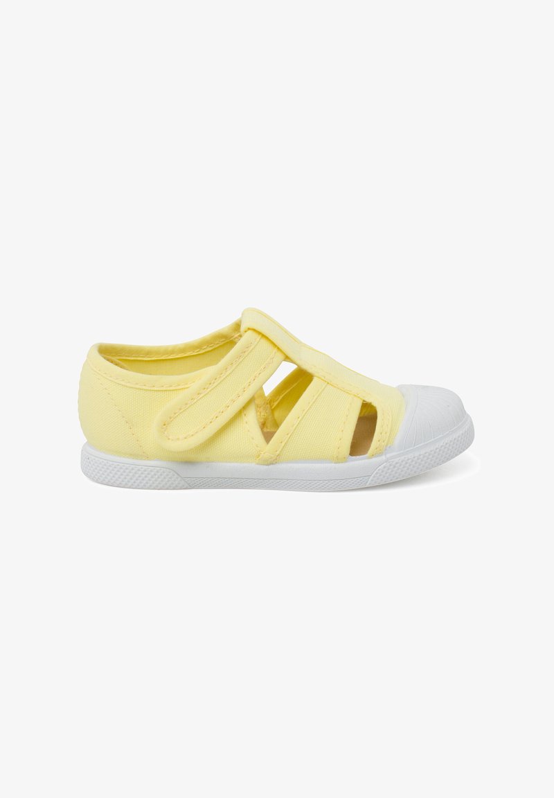Chaussure en tissu jaune avec des bandes Velcro, design découpé sur les côtés, et bout en cuir blanc et semelle en caoutchouc. Texture lisse, construction légère.