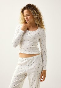 Vitt ribbat pyjamaset med blå blommönster, långa ärmar och rundad halsringning, samt figurnära byxor. Mjukt och lätt tyg.
