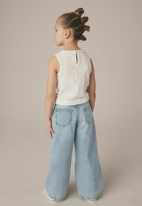 Vit, texturerad ärmlös topp med nyckelhål bak, ihopparad med vida ljusblå jeans som har två bakfickor och en avslappnad passform.