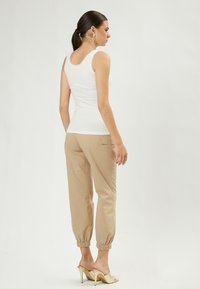 Top senza maniche bianco con bordo in pizzo abbinato a pantaloni joggers beige chiaro con polsini arricciati e mule con tacco aperto dorate.