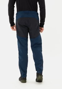 Marineblauwe outdoorbroek met zwarte accenten, voorzien van een getailleerde pasvorm, ritsopening aan de onderkant van de broekspijpen en duurzaam materiaal ontworpen voor actieve kleding.