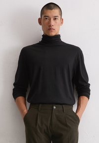 Czarny sweter z golfem, z długimi rękawami, o gładkiej teksturze. W połączeniu z oliwkowymi spodniami z jednym guzikiem. Minimalistyczny design.