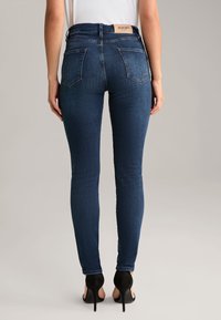 Ciemnoniebieskie skinny jeansy z wysokim stanem, detalami kieszeni z tyłu oraz metką z logo z tyłu. Gładka tekstura denimu. W połączeniu z czarnymi szpilkami.