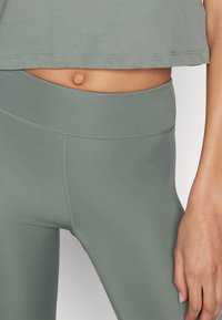 Leggings attivi verde chiaro con vita alta, texture liscia e cuciture piatte, abbinati a un top corto coordinato.