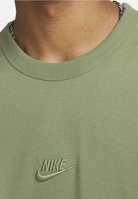 Olivově zelené bavlněné tričko s kulatým výstřihem a žebrovaným límečkem, s vyšívaným logem Nike ve shodné barvě. Měkká textura s uvolněným střihem.
