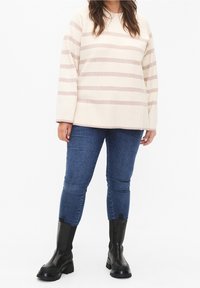 Maglione a righe color crema con linee orizzontali beige, abbinato a jeans skinny blu e stivaletti neri con suola spessa.