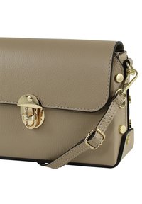 Beige leren handtas met een rechthoekige vorm, goudkleurige metalen details, magnetische sluiting en verstelbare riem; voorzien van decoratieve studs.