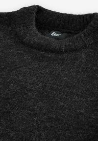 Gros plan d'un pull en maille noire duveteuse avec un col rond côtelé et une étiquette de marque noire visible à l'intérieur du col.