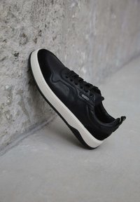 Černé kožené tenisky s bílou gumovou podrážkou, s plochými tkaničkami, polstrovaným límcem a malým logem na boku.