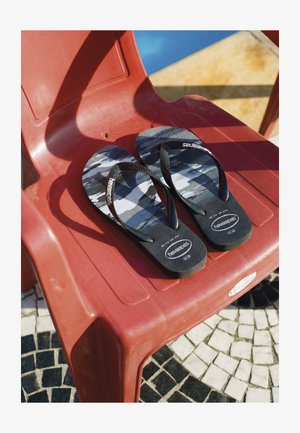 Schwarz-grau gemusterte Flip-Flops mit schwarzen Riemen auf einem roten Plastikstuhl auf Mosaikfliesenboden.