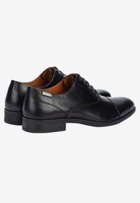 Zapatos de vestir de cuero negro con punta redonda, acabado suave y cierre de cordones; presentan un tacón bajo y un forro interior en contraste de color marrón.
