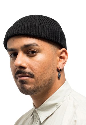 Bonnet en tricot noir à texture côtelée, porté sur une tête avec une barbe rasée de près. Boucle d'oreille en argent avec un pendentif arrondi détaillé.
