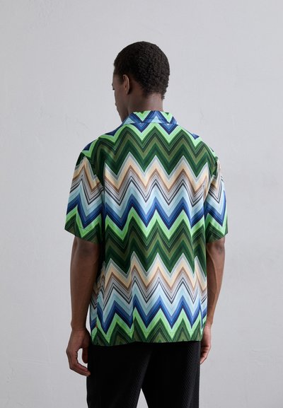 Chemise à manches courtes arborant un motif en zigzag dans des tons de vert, bleu et beige, fabriquée dans un tissu léger avec une coupe décontractée.