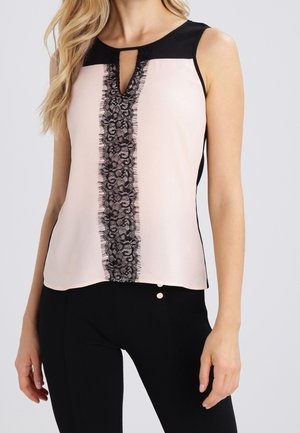 Bez rękawów bladoróżowy top z czarnym koronkowym pionowym paskiem i dekoltem w kształcie łezki, w połączeniu z dopasowanymi czarnymi spodniami z detalem w postaci złotych guzików.