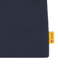 Tessuto blu navy con una trama testurizzata, caratterizzato da un'etichetta rossa e gialla nell'angolo. Il bordo è rifinito con un orlo pulito.