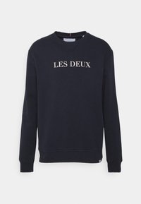 Sudadera azul marino oscuro hecha de tela suave, con cuello redondo y puños acanalados. En el frente aparece el texto "LES DEUX" en color crema.