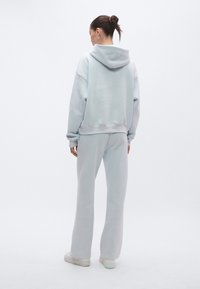 Sweatshirt azul claro com capuz e calças de fato de treino combinando, feitos de material macio com ajuste descontraído e detalhes canelados nos punhos e bainha.