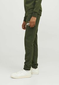 Grønne bomuldsjoggingbukser med slim fit, ribbede mansjetter og et logopatch på låret. Iført med hvide sneakers.