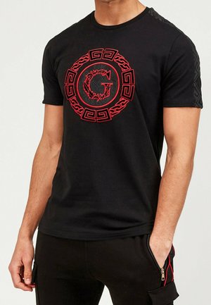 Sort kortærmet t-shirt med en fremtrædende rød cirkulær logo med et stiliseret 'G' og indviklede detaljer på skuldrene.