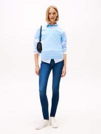 Light blue short-sleeve shirt with "Tommy Jeans" logo, layered over a white collared shirt, paired with dark skinny jeans and white sneakers.