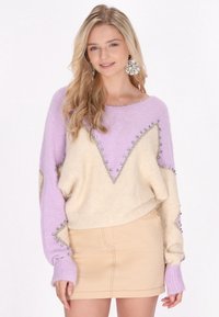 Strickpullover in Lavendel und Creme mit einem Chevron-Muster, verziert mit Perlen entlang der Säume. Kombiniert mit einem beigen Rock.