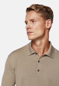 Polo shirt beige in maglia con colletto a risvolto, tre bottoni scuri e un tessuto texture. Adatto per un abbigliamento informale.