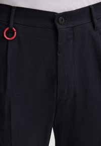 Pantalons bleu marine avec une finition texturée, dotés d'un bouton noir à la taille et d'un accent circulaire rouge.