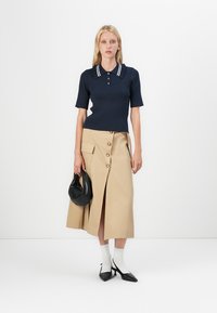 Marineblå ribbestrikket polo-skjorte med hvit krage, sammen med en beige midiskjørt med en frontsplitt og knappedetaljer. Svart håndveske og hæler.
