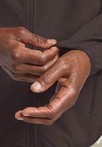 Veste marron foncé au design ajusté. Les mains ajustent le poignet de la manche, montrant une peau texturée et des coutures détaillées sur le tissu.
