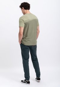 Camicetta verde oliva a maniche corte con una superficie liscia, abbinata a pantaloni blu scuro con orli e un dettagli rosso a contrasto.