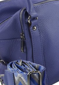 Paarse leren handtas met een gestructureerde afwerking, voorzien van zilverkleurige hardware, een ritssluiting en een blauw-grijs patroon op het hengsel.