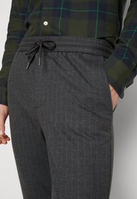 Grå pinstripede joggers lavet af blødt stof, med en elastisk talje med snor og sidelommer.